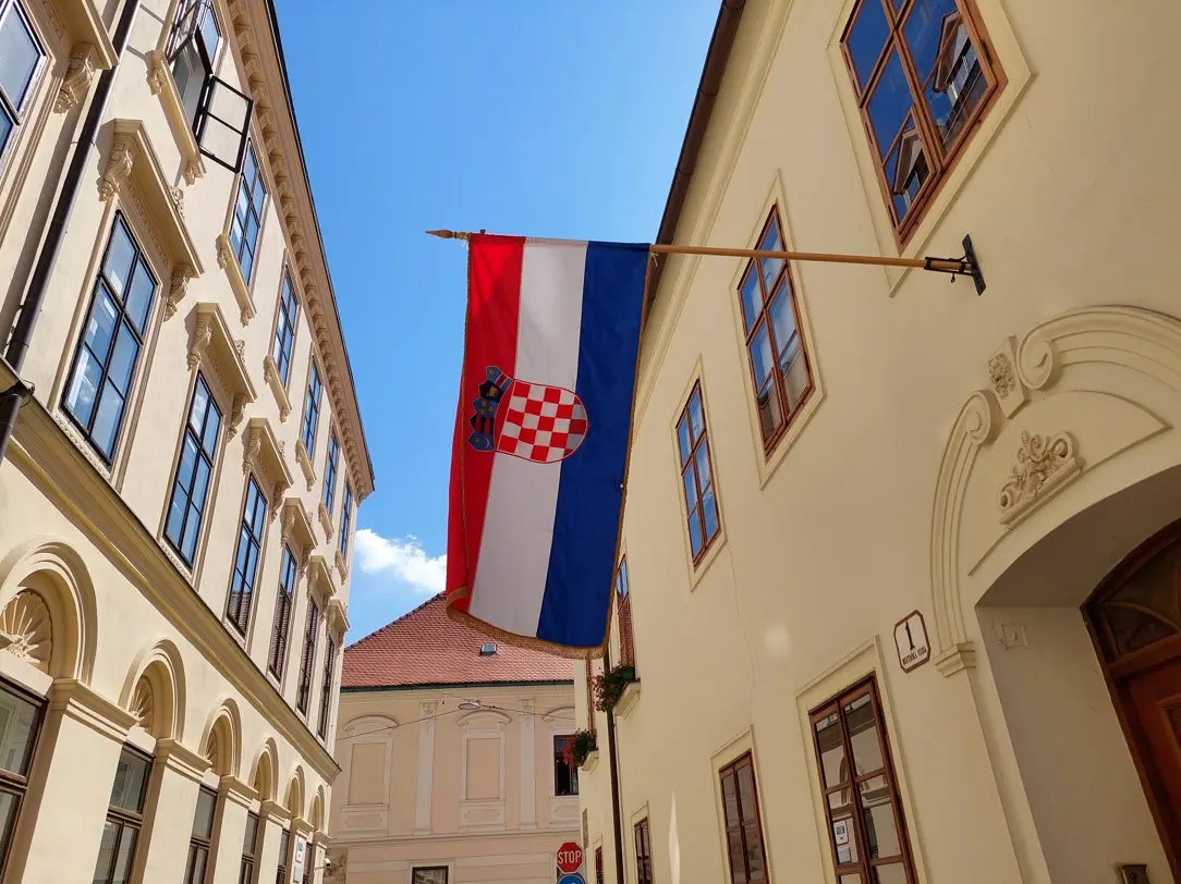 Hrvatska zastava vijori se između starih zgrada klasične arhitekture pod vedrim plavim nebom